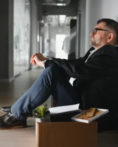 homme seul déprimé assis au sol dans son entreprise avec un carton rempli de ses affaires